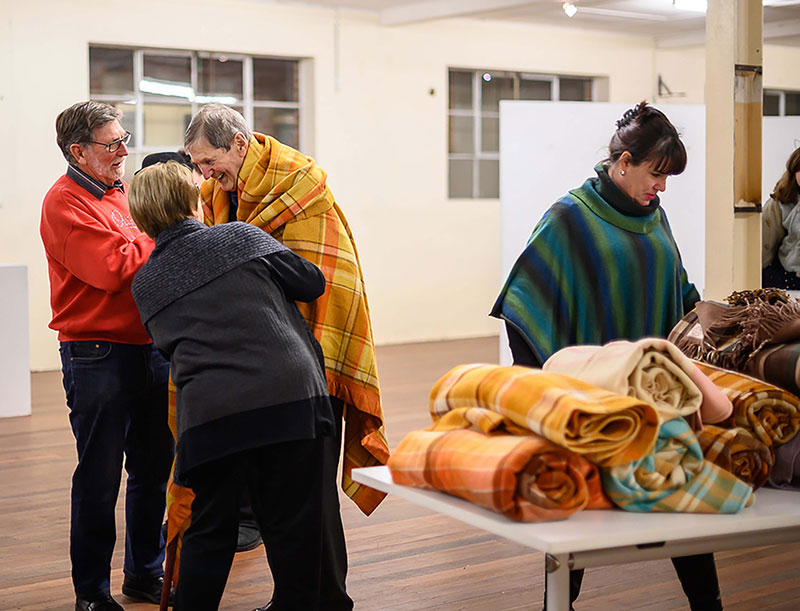 Image shows people standing near a table with blankets on it.