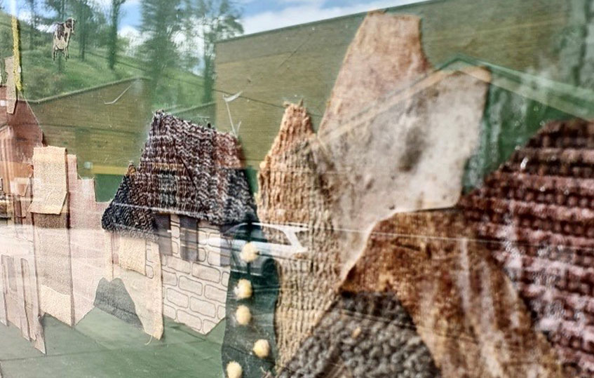 Image shows a close up of an artwork showing houses. Green fields are in the background.