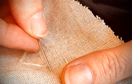 Image shows a close up of fingers stitching on beige material