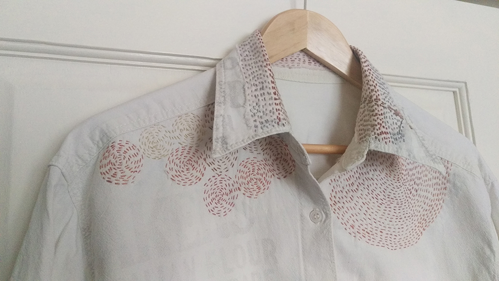 Image shows an embroidered shirt hanging on a wooden clothes hanger